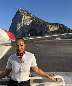 a woman standing next to an airplane with mountains in the backgrouds behind her