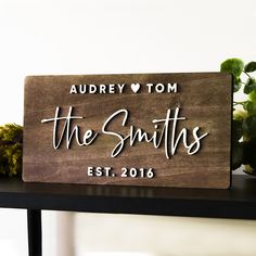 a wooden sign sitting on top of a table next to flowers and potted plants