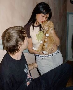 a woman holding an orange cat in her lap while another man looks at the camera