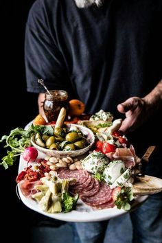 a man holding a platter full of different types of meats and cheeses