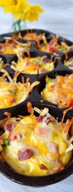 a muffin tin filled with breakfast food on top of a table next to a yellow flower