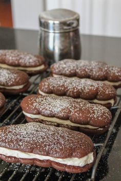 some cookies that are sitting on a cooling rack with powdered sugar and cream frosting