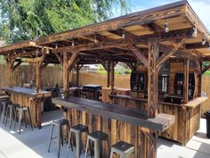 an outdoor bar with wooden tables and stools under a roof covered in wood planks