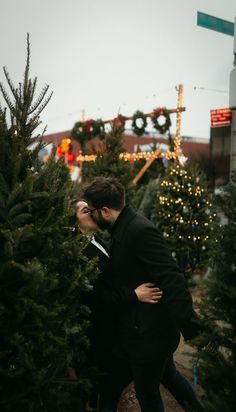 two people standing next to each other in front of christmas trees