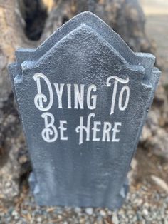 a tombstone with the words dying to be here painted on it's side in front of a tree