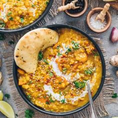 two bowls filled with yellow lentula soup next to sliced limes and pita bread