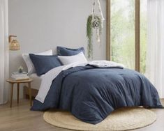 a bed with blue sheets and pillows in a white room next to a wooden floor