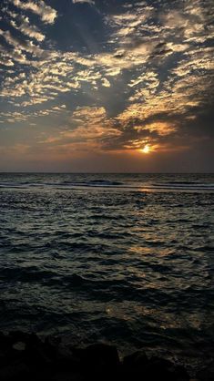 the sun is setting over the ocean with clouds in the sky and water below it