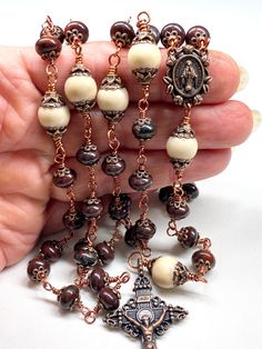 This five decade Catholic Rosary is made with 53 beautiful 8 mm Wine Color Poppy Jasper Rondelle beads, and 6 larger (10 mm) Cream Color Riverstone Beads (as the Our Father Beads). There are a total of 130 copper bead caps layered on the beads. This rosary is considered unbreakable due to the wire wrapping technique I use (not a simple loop, but wrapped around 3 times). The crucifix is a 2 Inch copper Crucifix, and is beautifully detailed. The center is a copper Miraculous Medal. JASPER: a semi- Handmade Artisan Rosary, Artisan Handmade Rosary, Chaplet Rosary, Poppy Jasper, Wire Wrapping Techniques, Rosary Prayer, Catholic Rosary, Rosary Catholic, Faith Prayer