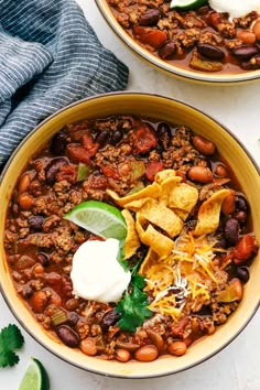 two bowls filled with chili, beans and tortilla chips on top of a white table