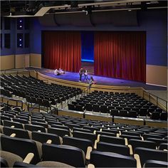 an empty auditorium filled with black chairs and red curtains