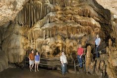 four people standing in front of a cave entrance with stalate formations on the walls