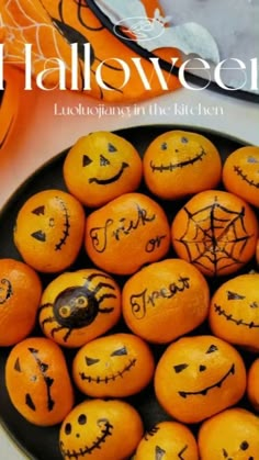 oranges with faces drawn on them are in a black bowl next to an orange pumpkin