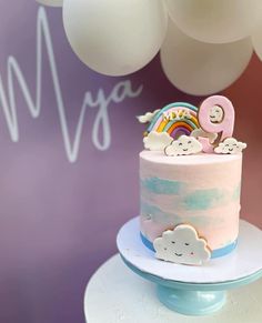 a pink cake with clouds and rainbows on top