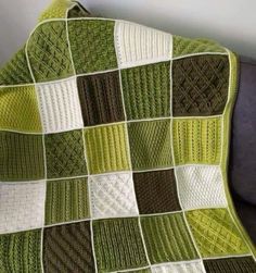 a green and white crocheted blanket sitting on top of a couch next to a wall