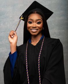 a woman wearing a graduation cap and gown posing for a photo in front of a gray background