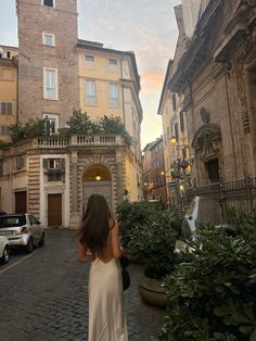 a woman is walking down the street in front of some buildings with cars parked on both sides