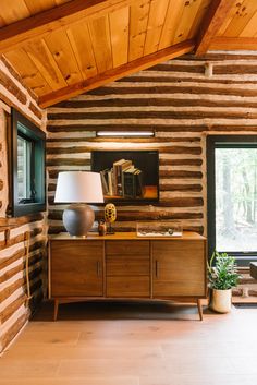 a living room with wood paneling and a lamp on top of the dresser next to a window