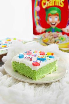 a green cake with white frosting and sprinkles on a plate next to a box of cereal