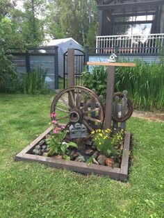 an old water wheel is in the middle of some flowers and rocks on the grass