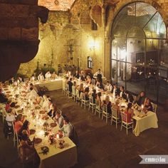 a large group of people sitting at tables in a room with tall ceilings and arched windows