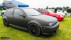 two cars parked next to each other on top of a grass covered field with people looking at them