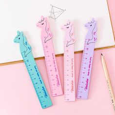 three different colored pencils and a ruler on a pink surface with a whiteboard in the background