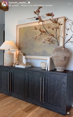 a vase sitting on top of a wooden cabinet next to a lamp and painting above it