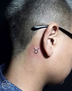 a man with a small tattoo on his ear and behind the ear is a pen