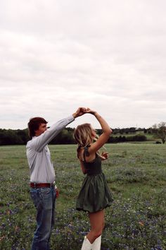 two people standing in a field, one holding the other's hand up to their head