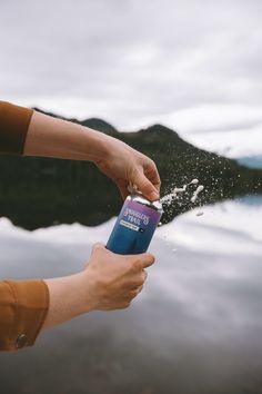 a person is spraying water onto their hand with a can in front of the lake