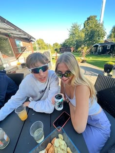 two people sitting at an outdoor table with food and drinks in front of their faces