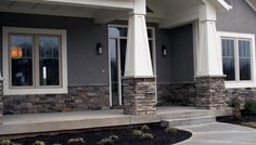 a gray house with white trim and stone pillars on the front porch is pictured in this image