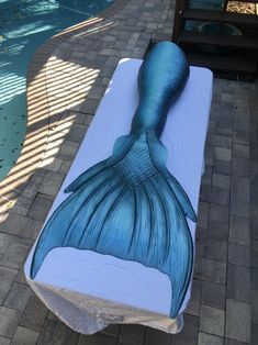 a large blue mermaid tail laying on top of a white sheet next to a swimming pool