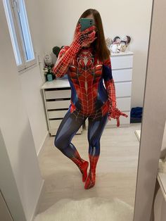 a woman in a spiderman costume taking a selfie with her cell phone while standing in the bathroom