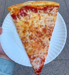 a slice of pizza on a paper plate being held up by someone's hand