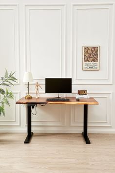 a desk with a computer on it in front of a white wall and potted plant