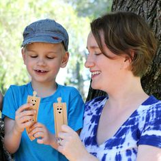 a woman and boy are playing with wooden toys in front of a tree, while another child looks on