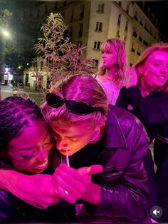 two women are hugging each other while one holds a lit candle in her hand and the other looks at her phone