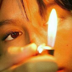 a person holding a lit candle in front of their face with one eye and the other hand