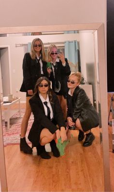 four women in suits and sunglasses taking a selfie with their cell phone while sitting on the floor