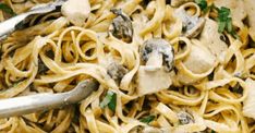 a bowl full of pasta with mushrooms and parmesan cheese on the side next to a pair of tongs