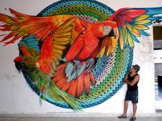 a woman standing in front of a colorful parrot mural