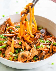 a bowl filled with noodles and meat being lifted by chopsticks from the bowl