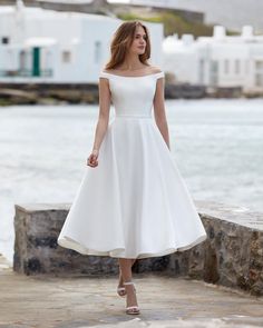 a woman in a white dress is standing near the water and looking off into the distance