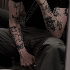 a man with tattoos on his arms sitting down and holding a cell phone to his ear