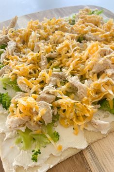 a pizza topped with cheese and broccoli on top of a wooden cutting board