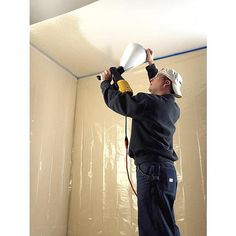 a man is painting the ceiling with white paint and a yellow sprayer on his head