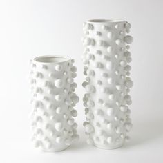 two white vases sitting next to each other on a white surface with small dots