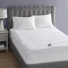 a white bed with three pillows on top of it and a night stand next to it